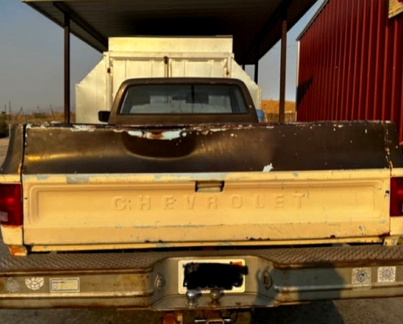 Square-body Chevy tailgate before: faded cream with peeling brown paint and a rusty bumper