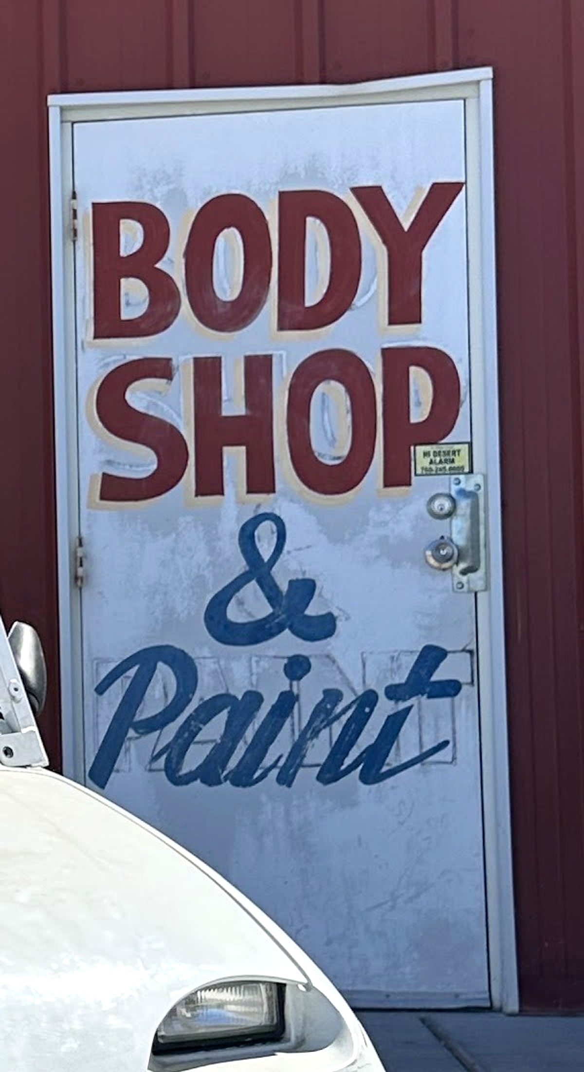 White steel door hand-painted with BODY SHOP in maroon and & Paint in navy script