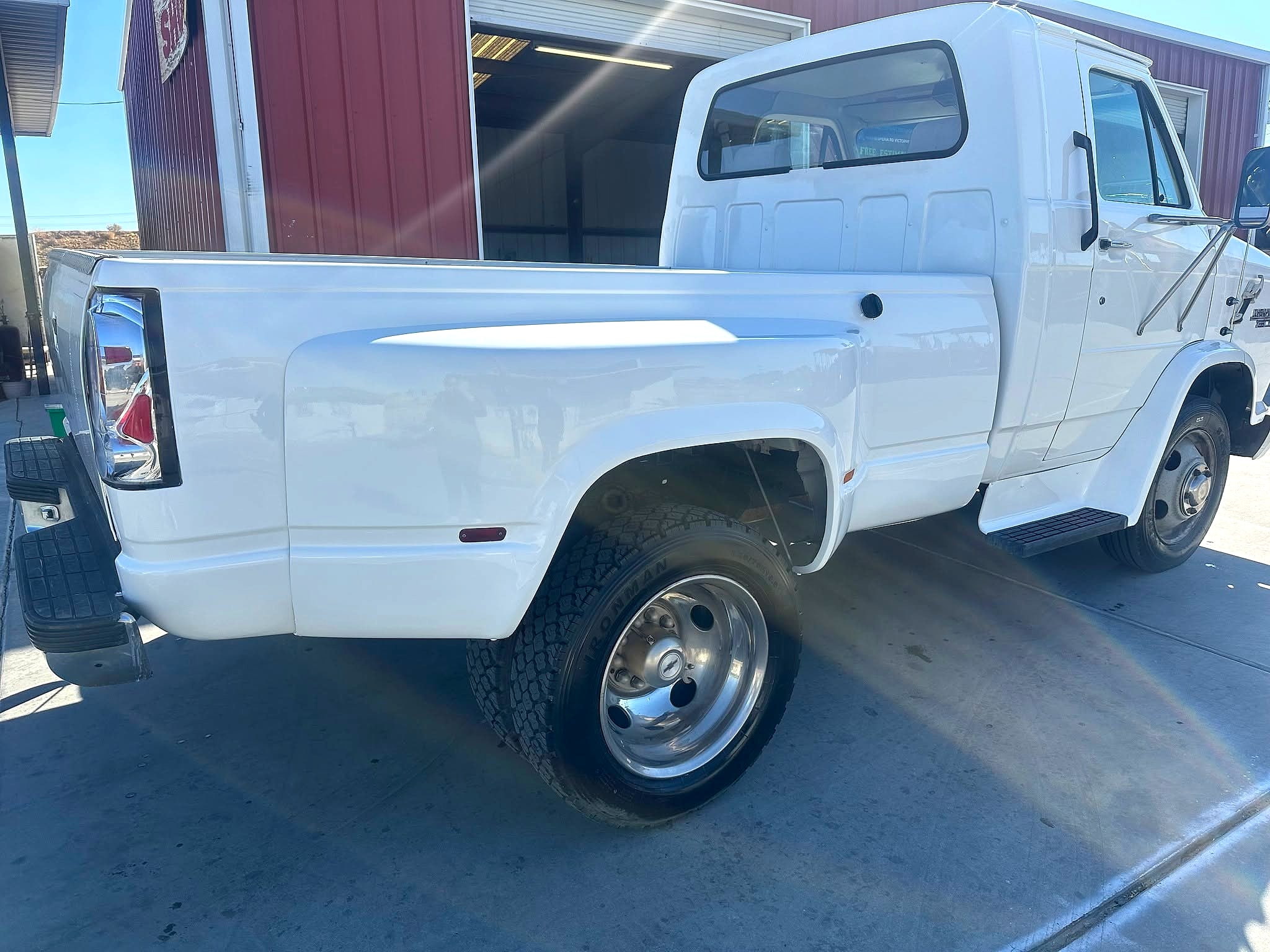 Finished white Chevy Van 30 HD dually from the rear three-quarter beside the barn-red shop