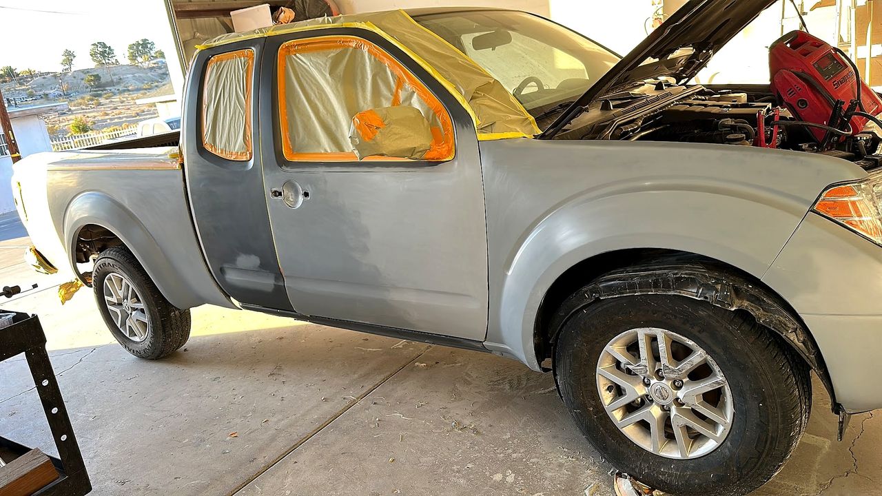 Silver Nissan Frontier with a primered door and masked windows inside the shop