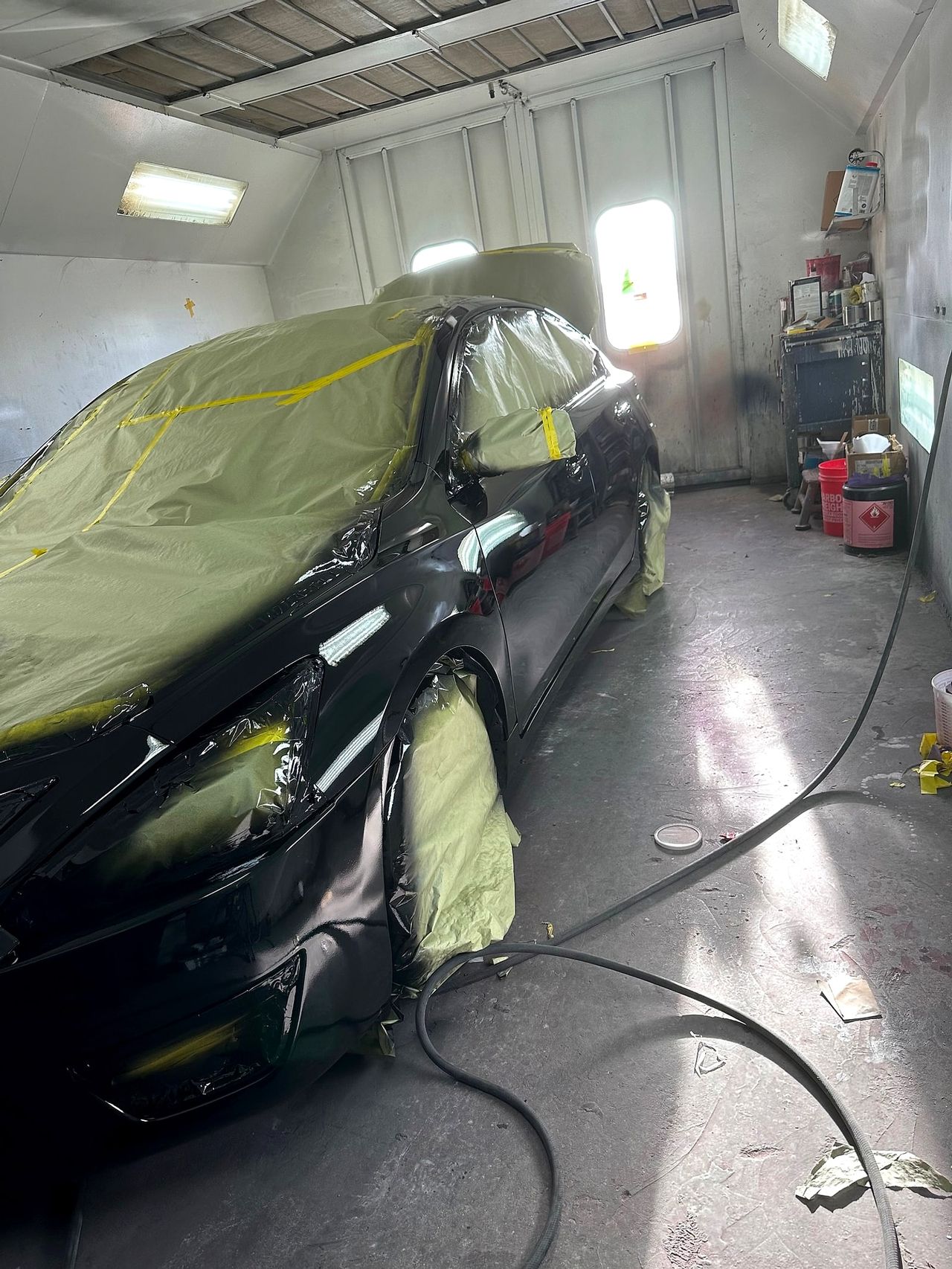 Black car masked in paper and plastic inside the paint booth