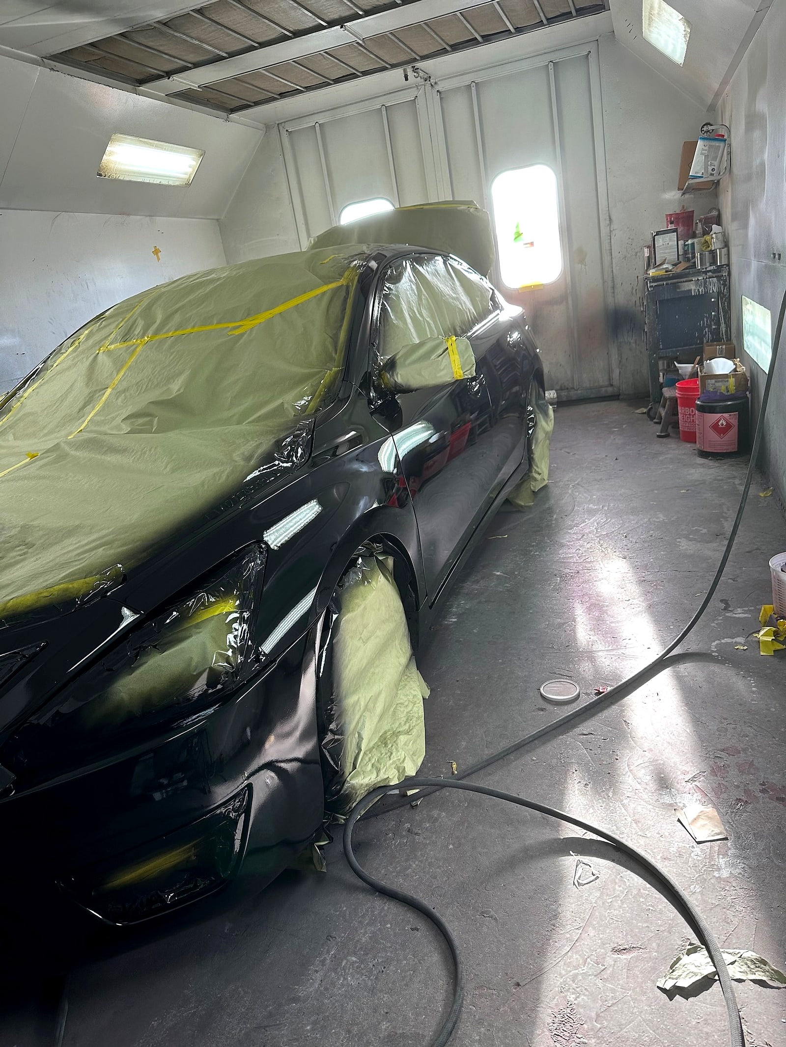 Black car masked in paper and plastic inside the paint booth