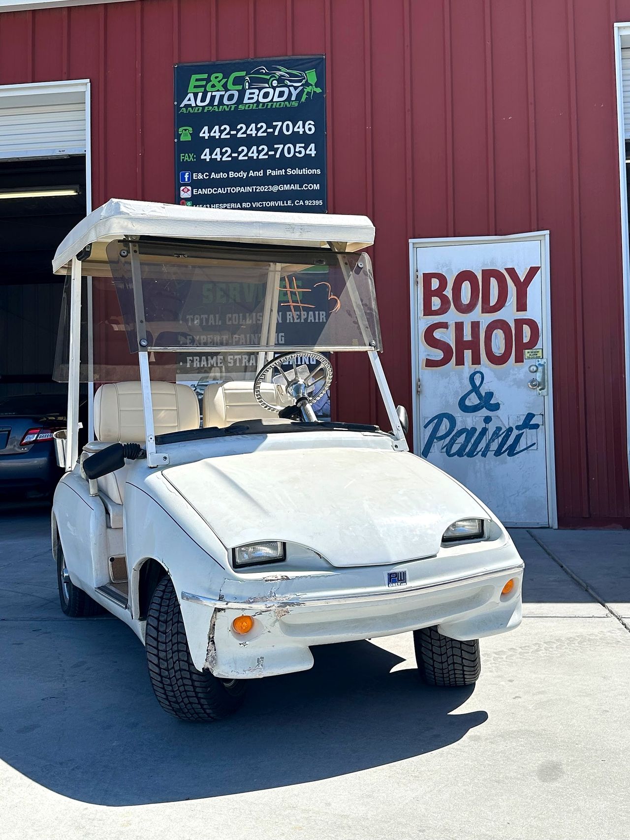 Golf cart with front-end damage parked in front of the E&C banner and the hand-painted door